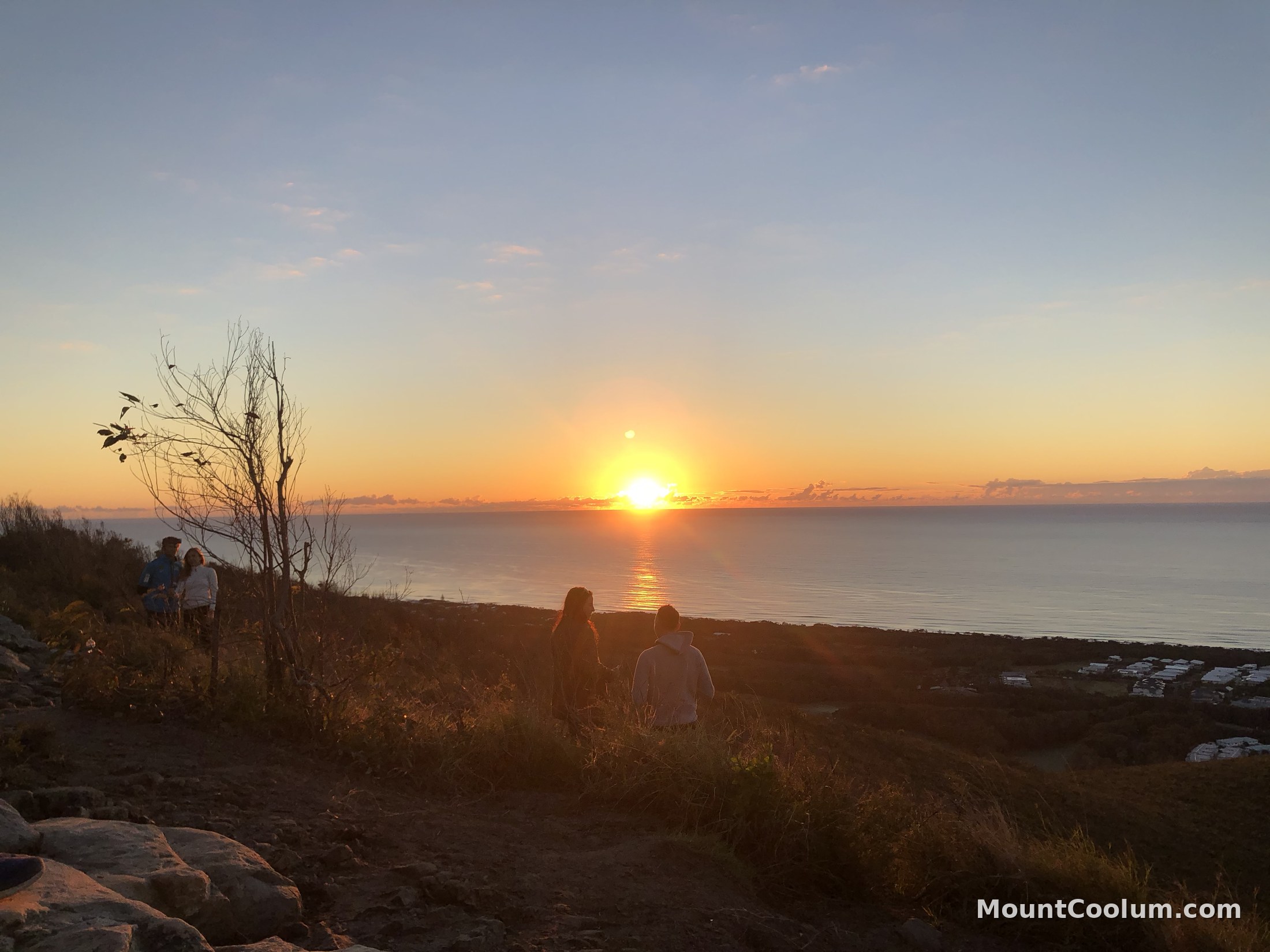 Walkers silhouetted against the sunset over the ocean from Mount Coolum, with the moon visible above