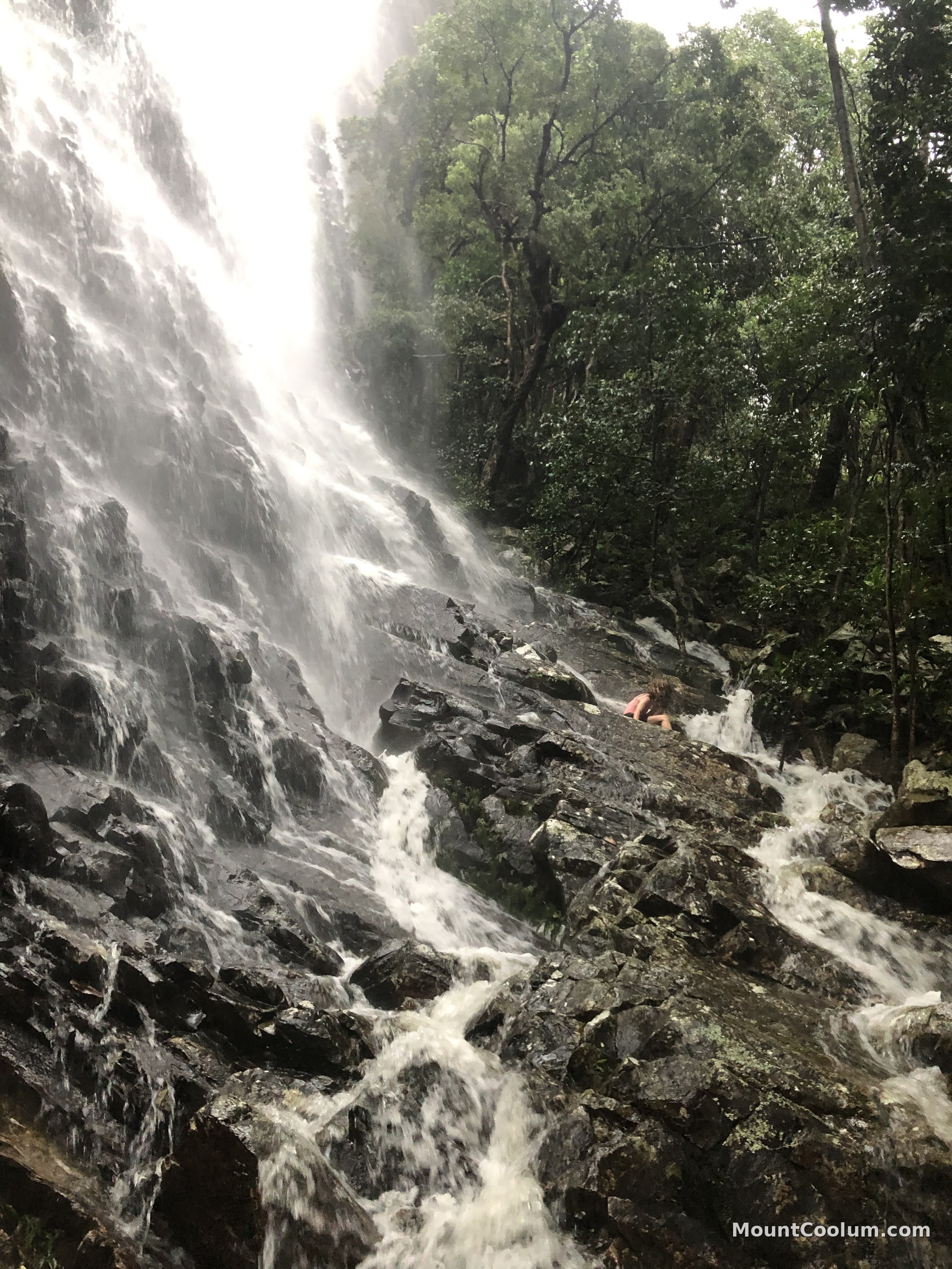 A child exploring the rocks beside a waterfall on Mount Coolum after rain